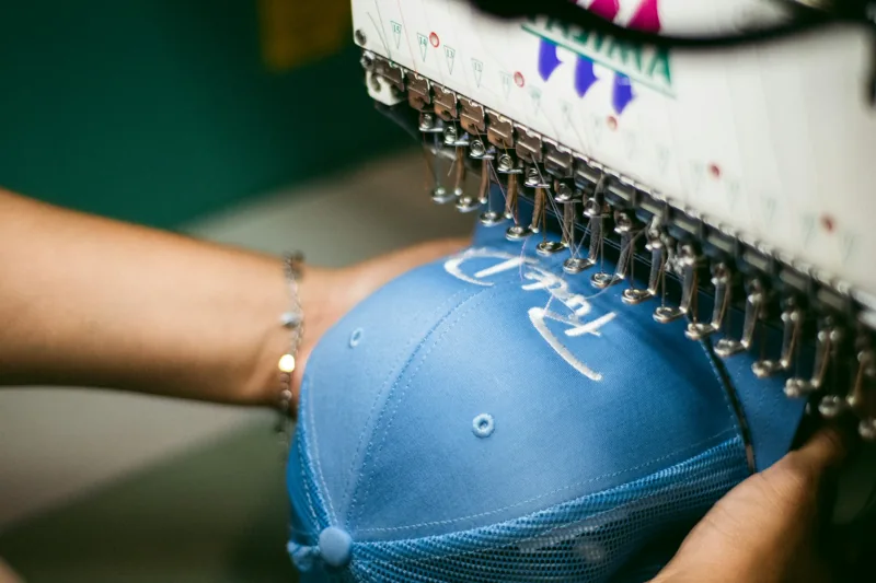 An embroidery machine stitching a design onto a blue cap